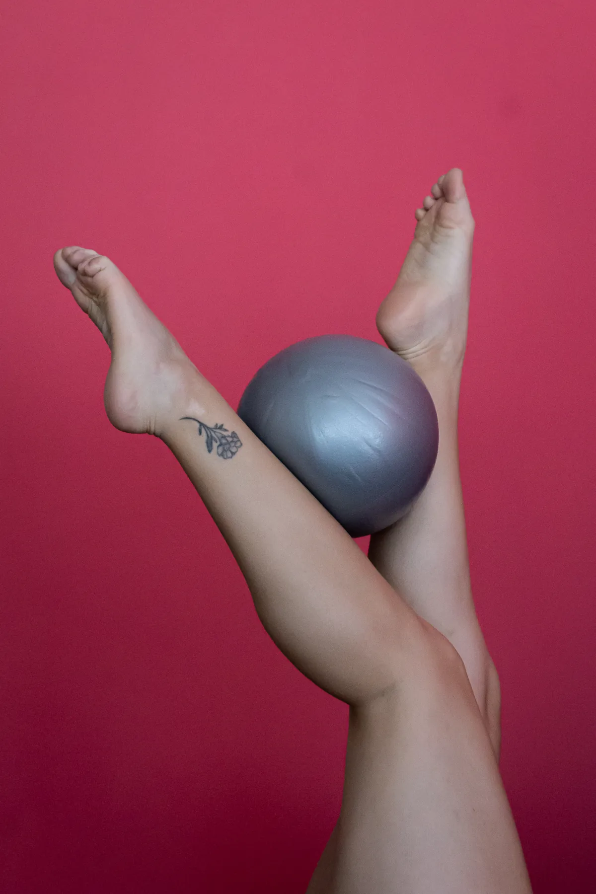 Piernas en alto que sostienen la pelota de Pilates, frente al muro rosado del estudio.